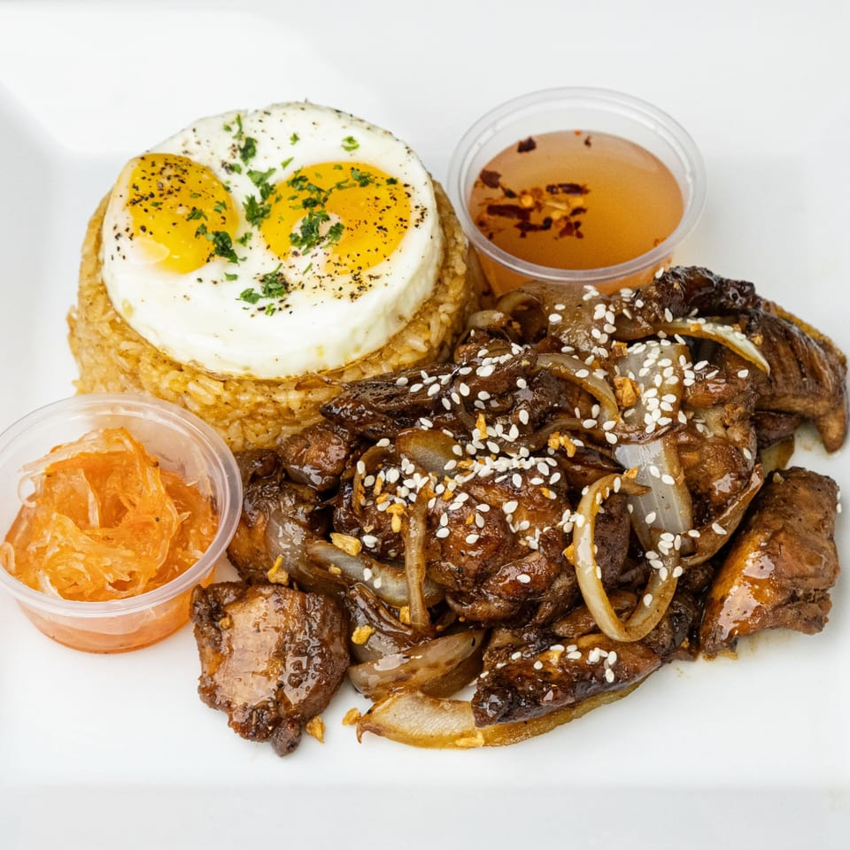 Plated beef with onions and sesame seeds, seasoned rice topped with two fried eggs, pickled vegetables, and dipping sauce.